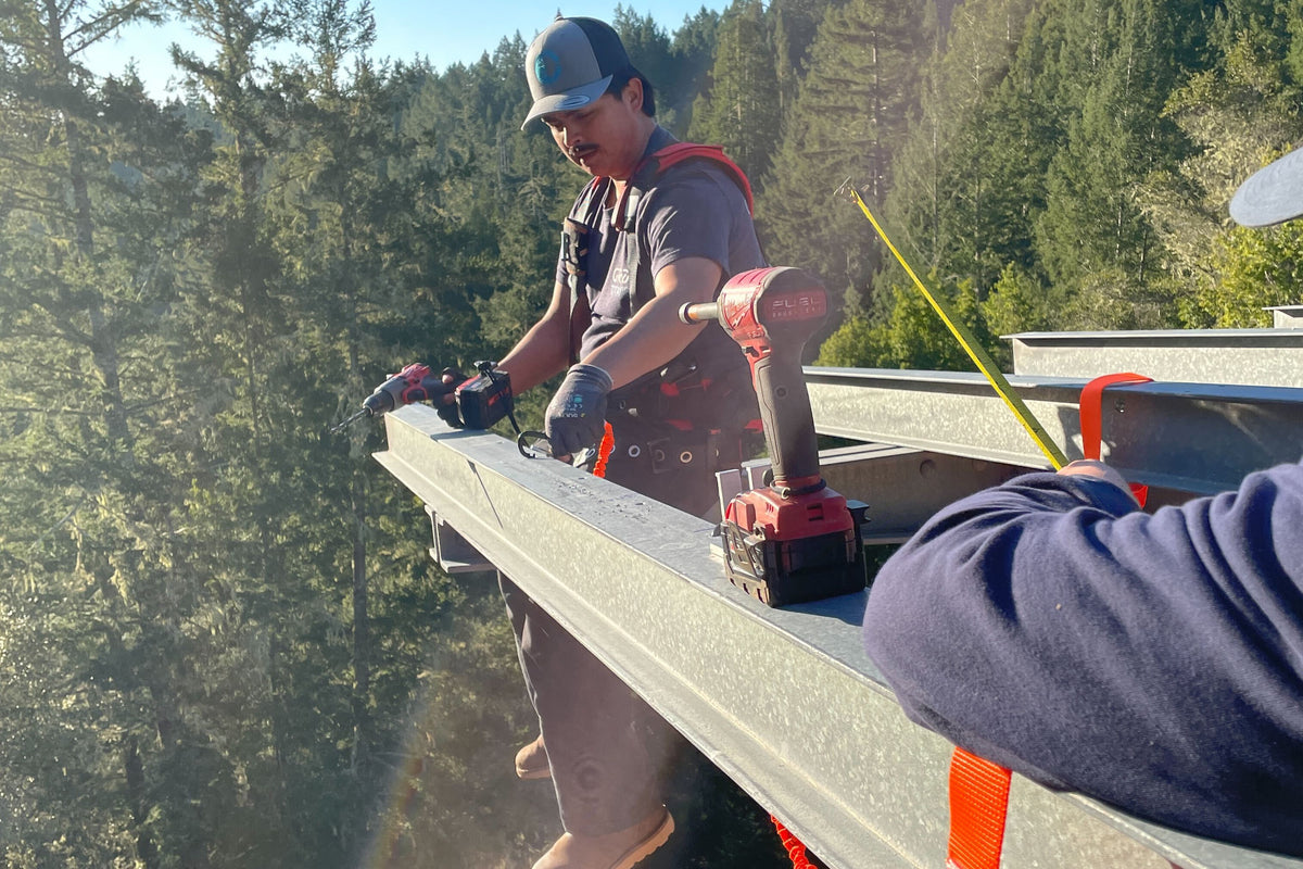 Person working on a roof with tools, surrounded by trees at Ratna Ling